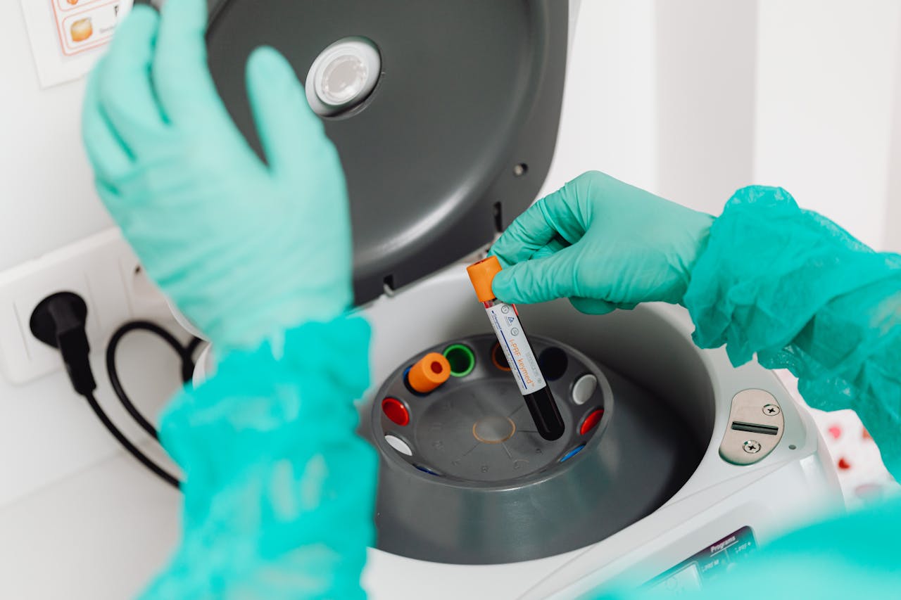 A lab technician wearing gloves uses a centrifuge for blood analysis in a modern laboratory setting.