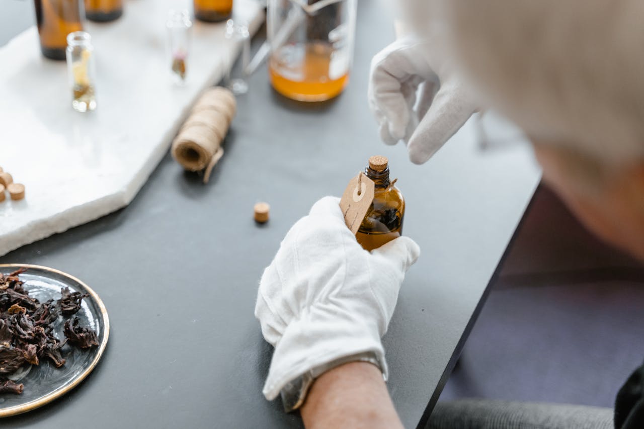 Person in gloves carefully handling aromatic compound in laboratory setting with various ingredients.
